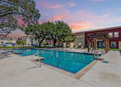 Thumbnail 30 of 39 - Affordable Apartments Near River Walk In N Park San Antonio, TX -The St. John - A Large Community Swimming Pool At Sunset With Arched Water Fountains And A Dark Wood Pergola.