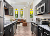Thumbnail 1 of 39 - Affordable Apartments Near Concepcion In Park San Antonio, TX - The St. John - A Galley-Style Kitchen With Cabinets, Granite Countertops, And A View Into A Living Area.