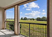 Thumbnail 12 of 33 - Apartments for Rent in Bentonville, AR 72713– Parc at Bentonville -   A balcony with a view of a grassy field and trees.