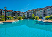 Thumbnail 22 of 33 - 1 & 2-Bedroom Apartments for Rent in Bentonville, AR – Parc at Bentonville – A large swimming pool with the apartments surrounding it and beach chairs