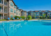 Thumbnail 23 of 33 - Pet-Friendly Rentals in Bentonville, AR – Parc at Bentonville – A large swimming pool with the apartments surrounding it and beach chairs