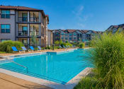 Thumbnail 2 of 33 - Pet-Friendly Rentals in Bentonville, AR – Parc at Bentonville – A large swimming pool with the apartments surrounding it and beach chairs