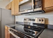 Thumbnail 4 of 25 - 1, 2 & 3-Bedroom Apartments for Rent in Maumelle, AR – Parc at Maumelle – A modern kitchen with a stainless steel stove and microwave above it.