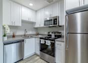 Thumbnail 1 of 15 - Two Bedroom Apartments in Hayward CA - Paseo Gardens - Modern Kitchen with Grey Countertops, White Cabinetry, Stainless Steel Appliances, and Wood Flooring