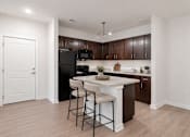 Thumbnail 1 of 14 - A kitchen with a black refrigerator and brown cabinets.