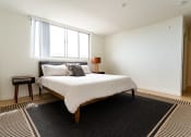 Thumbnail 7 of 29 - 1-Bedroom Apartments in Santa Monica, CA - San Vicente Tower - Furnished Bedroom with a Bed, Rug, Wood-Style Flooring, Wooden Nightstands, White Walls, and a Window