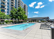 Thumbnail 17 of 21 - A swimming pool surrounded by lounge chairs and trees in front of a building.