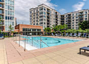 Thumbnail 11 of 25 - A swimming pool surrounded by lounge chairs and a building in the background.