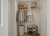 Thumbnail 9 of 31 - A white closet with clothes hanging and shoes on a shelf.