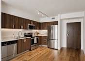 Thumbnail 5 of 31 - Modern kitchen with stainless steel appliances, quartz countertops, and wood-style cabinetry inside a one-bedroom apartment at Riverview One Apartments in Downtown Miami.