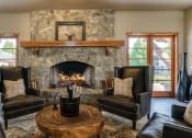 Thumbnail 4 of 26 - Apartments In Coeur d'Alene, ID - Rockwood Lodge - Resident Clubroom With Wood-Style Flooring, Area Rug, Leather Armchairs, Coffee Table, And Fireplace.