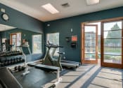Thumbnail 11 of 26 - Two Bedroom Apartments in Coeur d’Alene ID - Rockwood Lodge - Fitness Center with Exercise Equipment, Weights, a Large Window, and a Door with Pool Access