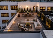 Thumbnail 10 of 25 - A rooftop patio with a couch, chairs, and string lights.