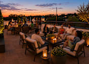 Thumbnail 12 of 25 - A group of people are sitting around a table on a deck with a beautiful sunset in the background.