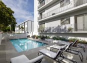 Thumbnail 17 of 29 - Two BR Apartments in Santa Monica CA - San Vicente Tower - Sparkling Pool Surrounded by Lounge Seating and View of Apartment Building