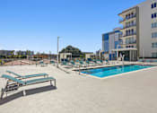 Thumbnail 13 of 27 - Apartments for Rent in Riverview Miami, FL– Riverview One Apartments -   A large swimming pool with sun loungers and a building in the background.