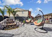 Thumbnail 13 of 25 - A patio with two hanging chairs and a fire pit.