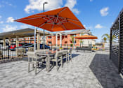 Thumbnail 17 of 25 - A patio with a table and chairs under an orange umbrella.