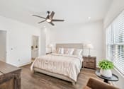 Thumbnail 11 of 39 - A bedroom with a large bed, a ceiling fan, and a small table with a plant on it.