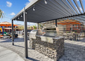 Thumbnail 22 of 25 - A stone grill is on a patio under a metal roof.