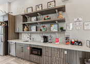 Thumbnail 24 of 28 - A kitchen with a refrigerator, microwave, and shelves with various items.