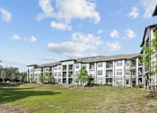 Thumbnail 6 of 28 - A large apartment complex with a grassy area in front.