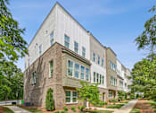 Thumbnail 37 of 39 - A modern building with a mix of white and brown exterior walls, surrounded by greenery and a clear blue sky.