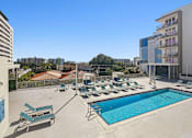 Thumbnail 12 of 27 - 1- & 2-Bedroom Apartments for Rent in Miami, FL – Riverview One Apartments – A swimming pool with sun loungers and apartment buildings in the background.