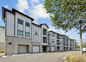 Thumbnail 23 of 28 - A modern apartment building with a parking lot in front.