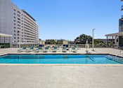 Thumbnail 1 of 27 - Pet-Friendly Rentals in Miami River, FL – Riverview One Apartments – A large swimming pool surrounded by lounge chairs and a white building in the background.