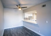 Thumbnail 25 of 31 - an empty room with a ceiling fan and a kitchen in the background
