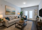Thumbnail 5 of 23 - A living room with a beige couch, a coffee table, and a painting on the wall.