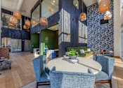 Thumbnail 19 of 28 - a communal area with a round table with blue chairs and a green couch in the background