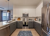 Thumbnail 8 of 28 - Three-Bedroom Apartments in Old East Dallas, TX - 4600 Ross - Kitchen with Hardwood-Style Flooring, Stainless Steel Appliances, Two-Tone Cabinets, Designer Kitchen Tile Backsplash, and Spacious Quartz Countertops.
