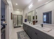 Thumbnail 9 of 28 - One-Bedroom Apartments in Old East Dallas, TX - 4600 Ross - Bathroom with Dual Sink Vanity, Quartz Countertop, Dual Large Mirrors, Tile Flooring, and Walk-In Shower with Sliding Glass Door.