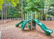 Thumbnail 4 of 19 - A green slide in a playground surrounded by trees.