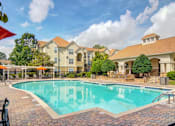 Thumbnail 2 of 19 - Pet-Friendly Apartments in Duluth– Grande Club – A large swimming pool in front of a building with a patio and umbrellas.