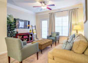Thumbnail 9 of 19 - A living room with a green chair, a brown ottoman, and a yellow couch.