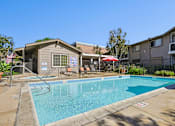 Thumbnail 2 of 21 - Community pool area with lounge chairs and mature landscaping at Sunnyside Senior Apartments in San Dimas, CA