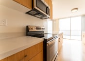 Thumbnail 5 of 29 - Santa Monica, CA Apartments near Dodger Stadium - San Vicente Tower - Modern Kitchen with Wood-Style Cabinetry, White Quartz Countertops, with a Stainless Steel Microwave, a Stove, and an Oven