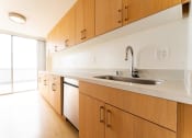 Thumbnail 3 of 29 - Apartments for Rent in Santa Monica, CA - San Vicente Tower - Kitchen with Wood Cabinets, Stainless Steel Appliances, Hardwood Flooring, Large Sliding Glass Door, and White Countertops