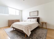Thumbnail 6 of 29 - One, Two, and Three-BR Apartments in Santa Monica, CA - San Vicente Tower - Bedroom with Large Window, Hardwood Flooring, Bed, Dresser, and Large Window