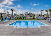 Thumbnail 6 of 36 - A large swimming pool surrounded by lounge chairs and palm trees.