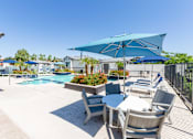 Thumbnail 41 of 55 - A pool area with a table and chairs under a blue umbrella.
