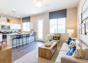 Thumbnail 3 of 55 - Phoenix, AZ, Apartments near Westgate - The Crofton - Open-Concept Living Room and Kitchen with Breakfast Bar Seating, Blue Stools, Cozy Sofa, Wood Coffee Table, and Large Windows with Soft Light.
