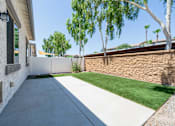 Thumbnail 24 of 55 - A concrete walkway leads to a house with a stone wall and green grass.