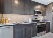 Thumbnail 9 of 50 - Apartments For Rent In Greenwood, WA - The Morrow - Fully Equipped Kitchen With Stainless Steel Appliances, Wooden Cabinets, Tile Backsplash, Granite Counters, And Vinyl Plank Flooring