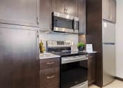 Thumbnail 6 of 50 - Apartments in Greenwood for Rent - The Morrow Fully-Equipped Kitchen with Stainless Steel Appliances, Dark Cabinetry, Subway Style Backsplash, and Vinyl Plank Flooring