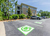 Thumbnail 22 of 32 - A parking lot with a green electric car charging station sign.