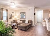 Thumbnail 7 of 24 - Opelika, AL Apartments – The Crossings of Opelika - a living room with a couch and a table with hardwood floors and a ceiling fan